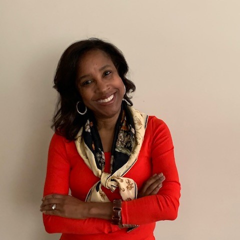 A headshot of Allison Simmons folding her arms against a neutral beige background.