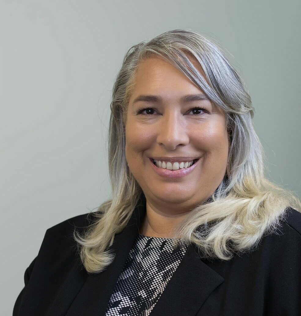 A headshot of Antonia Carew-Watts against a neutral grey background.