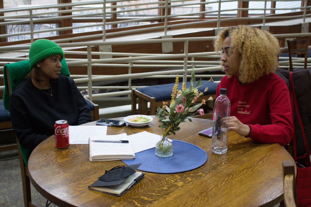 Resita Cox and Ashley O'Shea are sitting and talking to each other at a one of the tables in the Edith Macy Center lounge.
